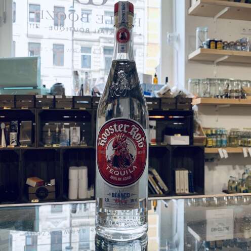 Produktbild Rooster Rojo Blanco Tequila Alt Attribut Rooster Rojo Blanco Tequila kaufen bei Belle Booze Tequila Glas mit klarer Farbe und Limette Alt Attribut Rooster Rojo Blanco frische Agave im Glas Flasche vor Agavenfeld Kulisse Alt Attribut Rooster Rojo Blanco Tequila aus Jalisco Mexiko